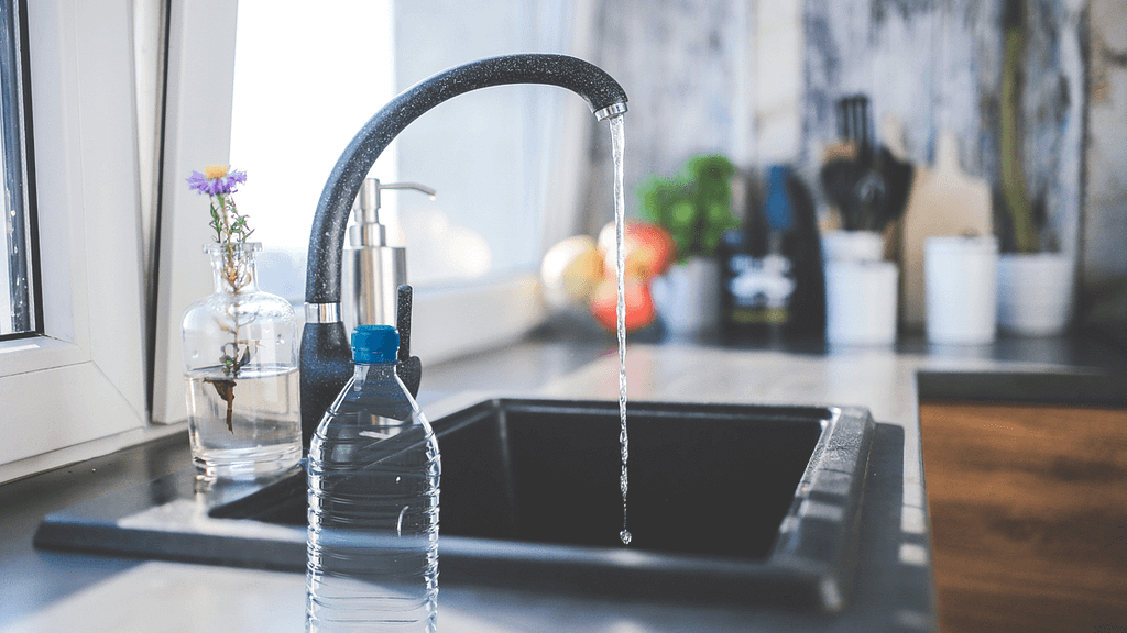 Photo of running faucet water with bottled alongside on kitchen counter